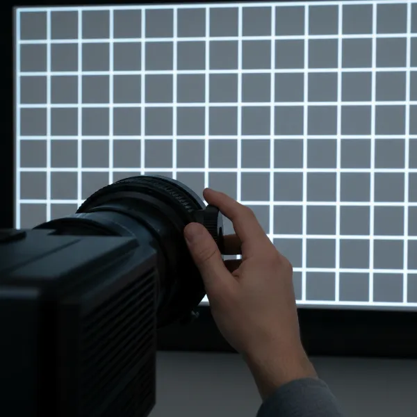A close-up shot of a hand carefully turning the focus ring on a projector lens, with a crisp, clear projected test pattern in the background.